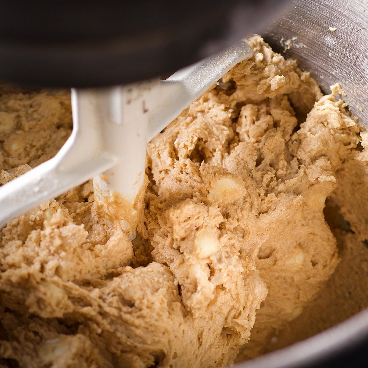 A stand mixer slowly mixing white chocolate chips into cookie dough.