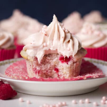A raspberry cupcake topped with raspberry cream cheese buttercream with a bite taken out of it.