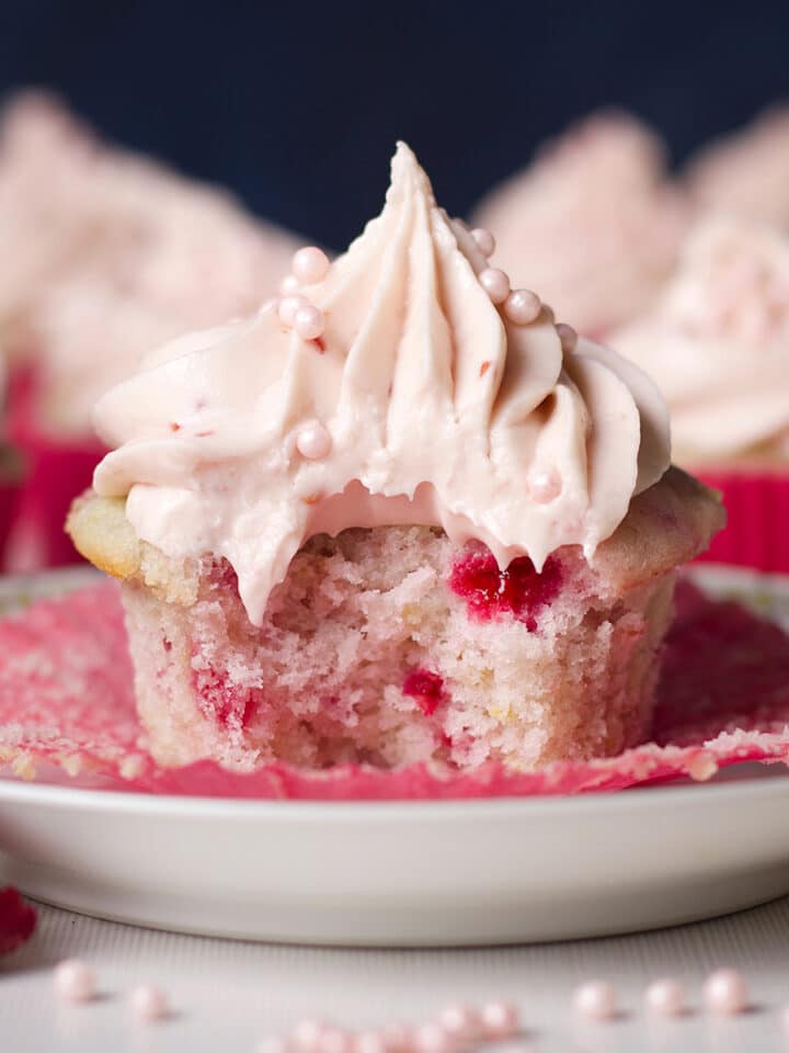 A raspberry cupcake topped with raspberry cream cheese buttercream with a bite taken out of it.