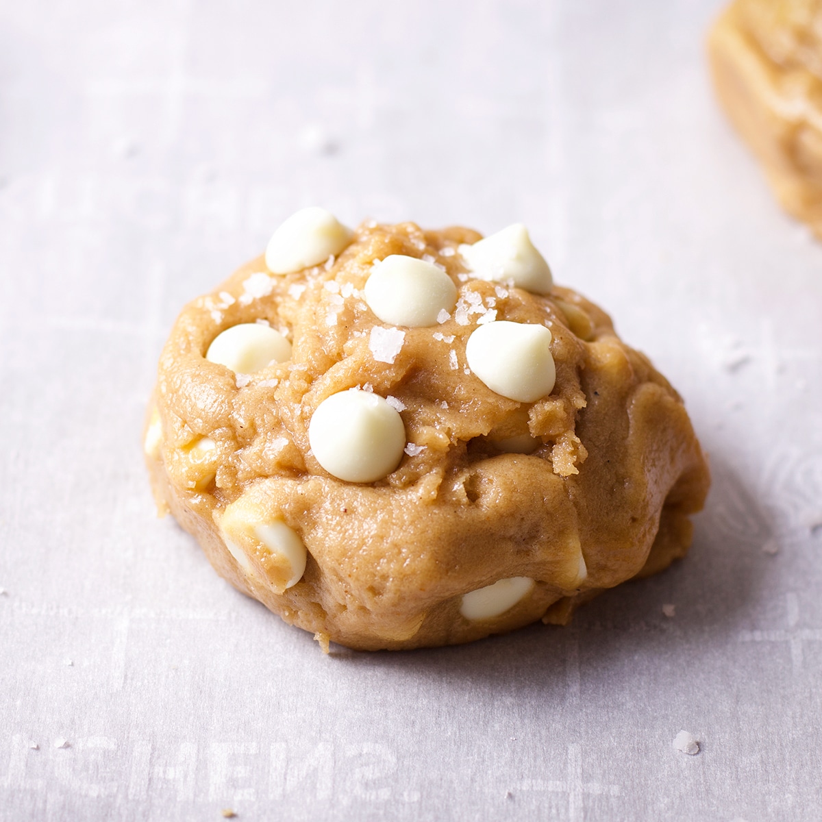 A ball of white chocolate chip cookie dough with white chocolate chips and salt pressed into the top.