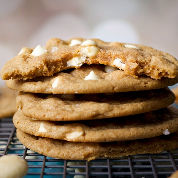 A stack of white chocolate chip cookies with a bite taken out of the top cookie.