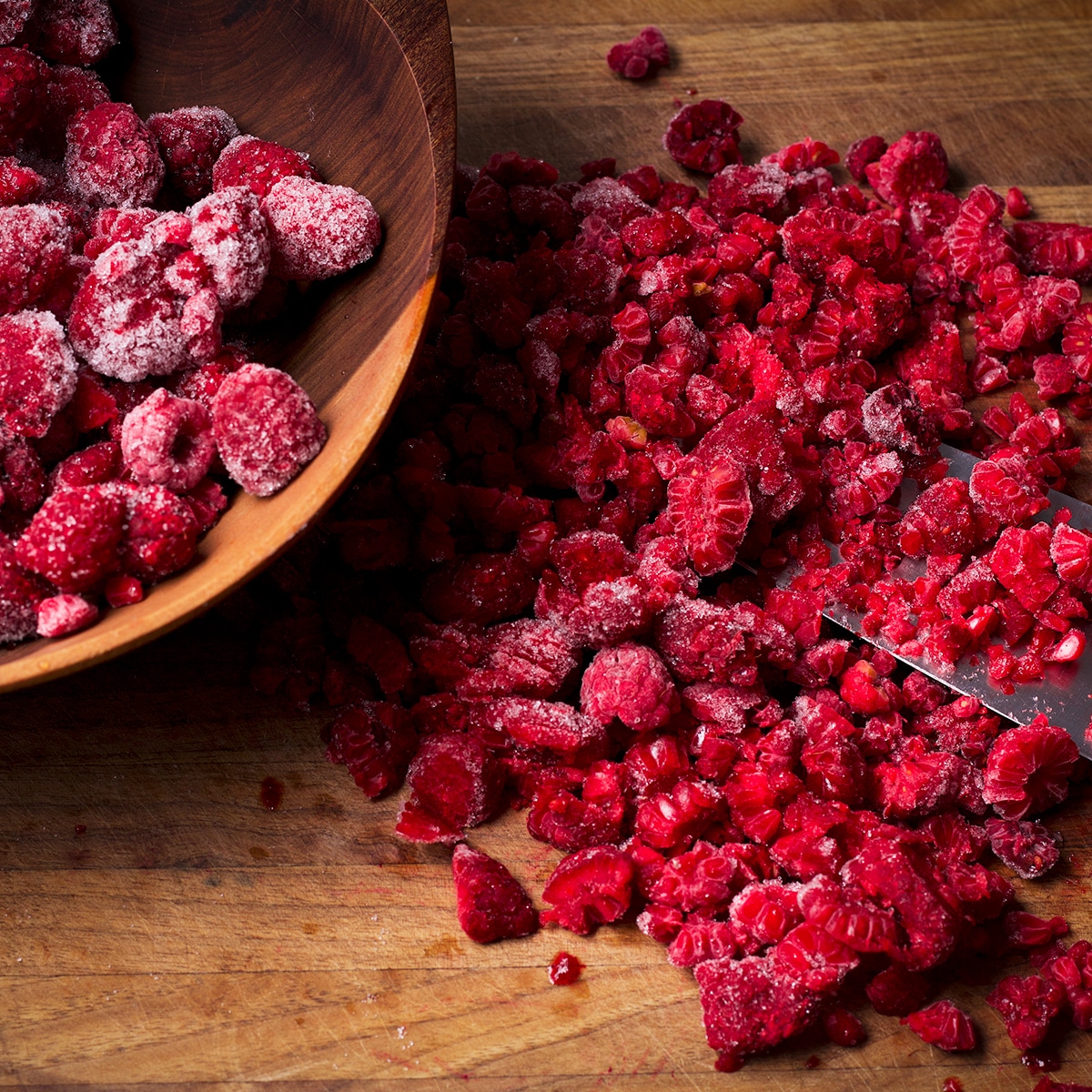 Chopping frozen raspberries into small pieces on a wood cutting board.