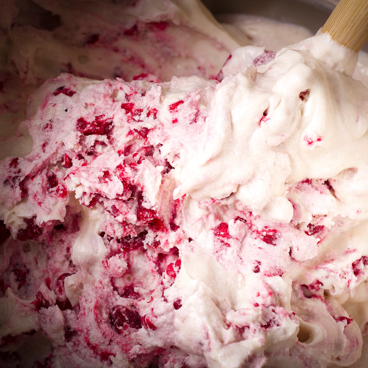 Using a rubber spatula to gently fold frozen chopped raspberries into cupcake batter.