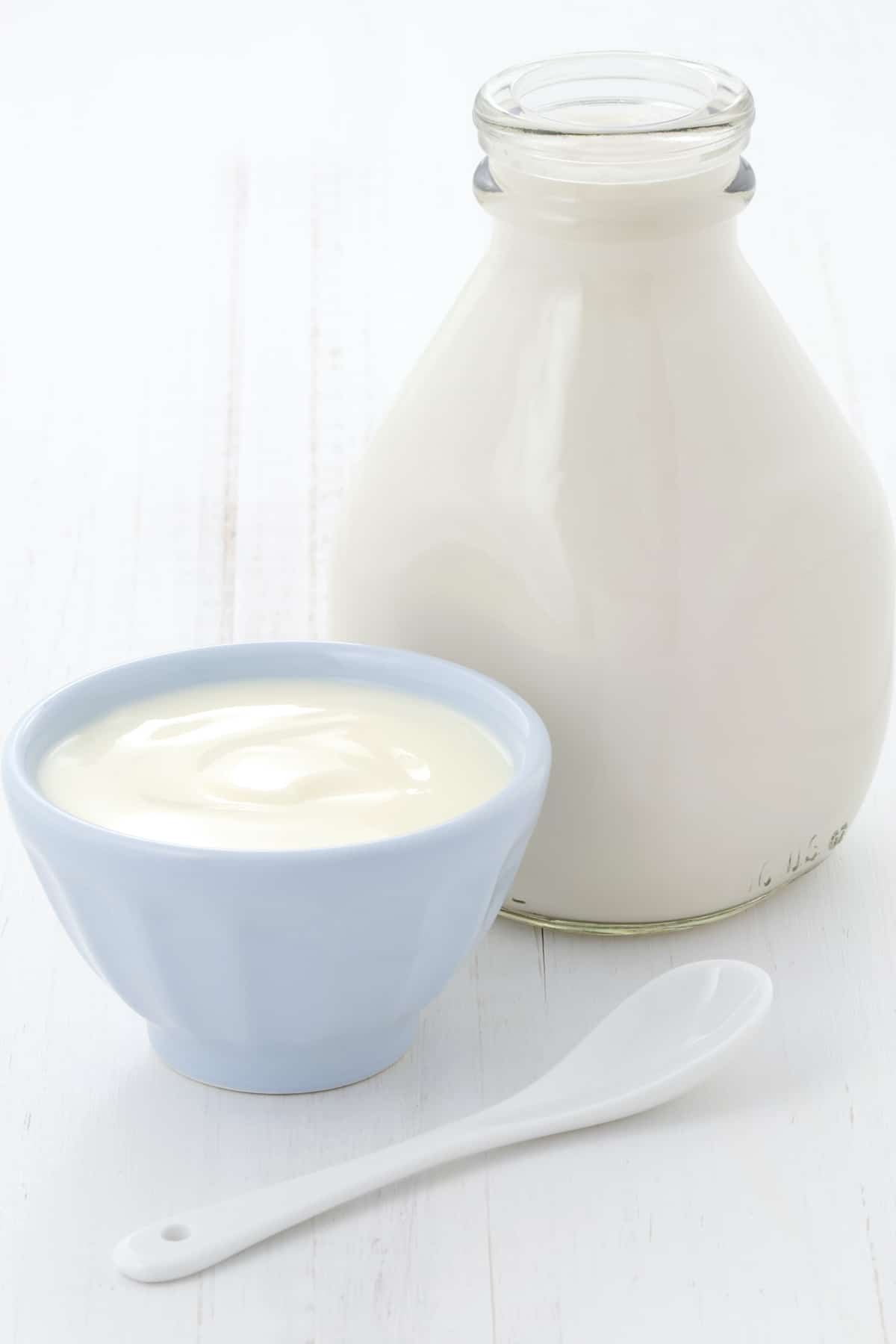 A glass bottle of milk next to a small dish of yogurt.