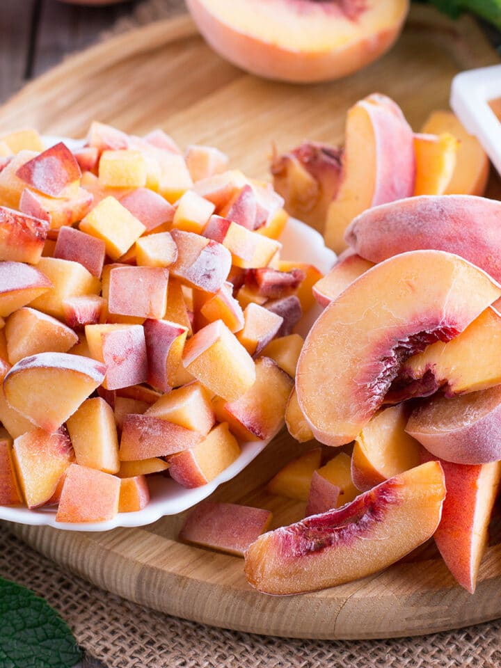 A bowl of frozen peach chunks next to sliced frozen peaches and an ice cube tray filled with frozen peach puree.