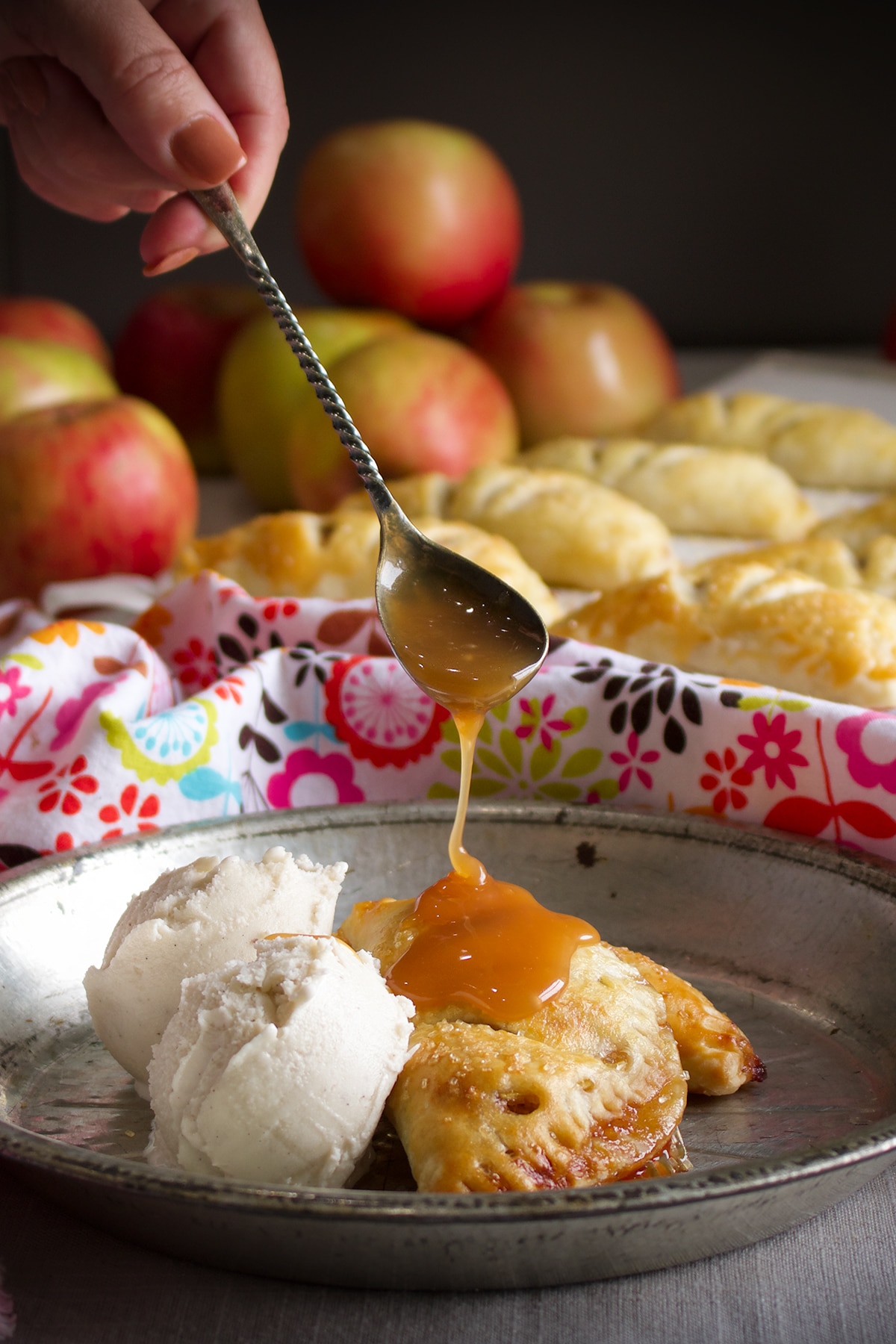 Using a spoon to drizzle salted caramel sauce over two apple butter hand pies on a tin plate.