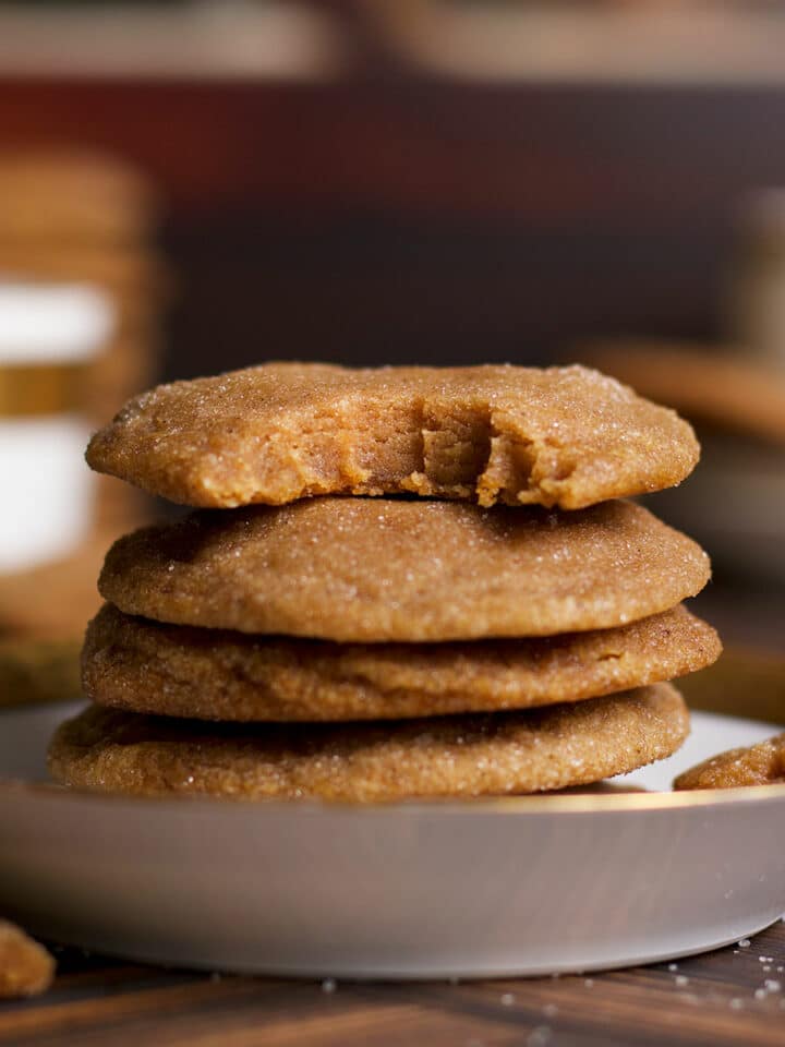 Several brown sugar cookies on a plate with a bite taken out of the cookie on the top of the pile.