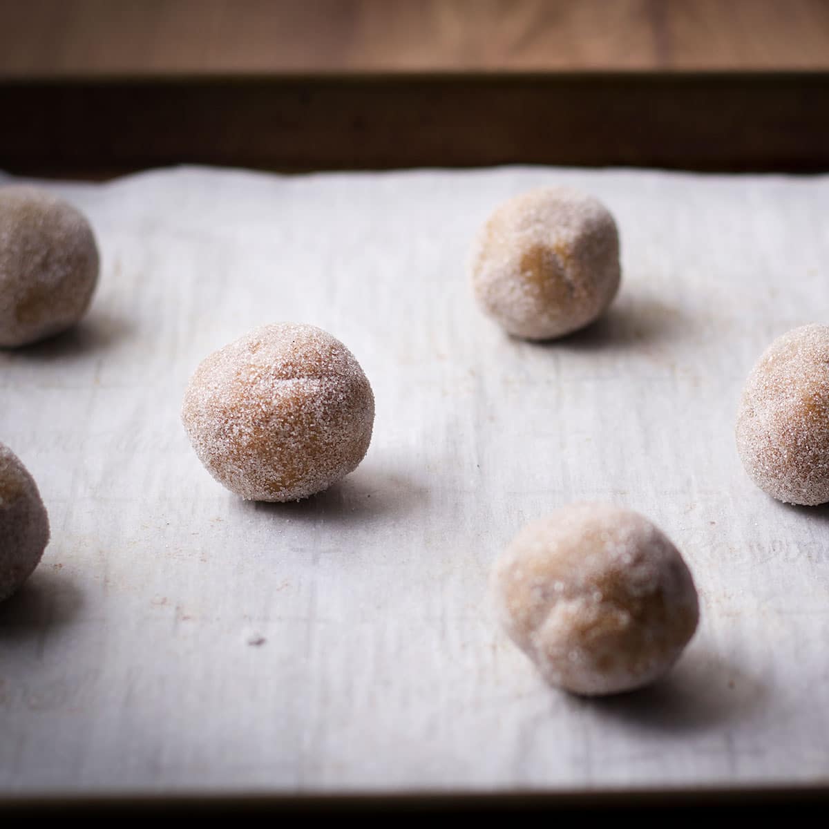 Balls of brown sugar cookie dough that have been rolled in sugar and placed on a parchment paper lined cookie sheet.