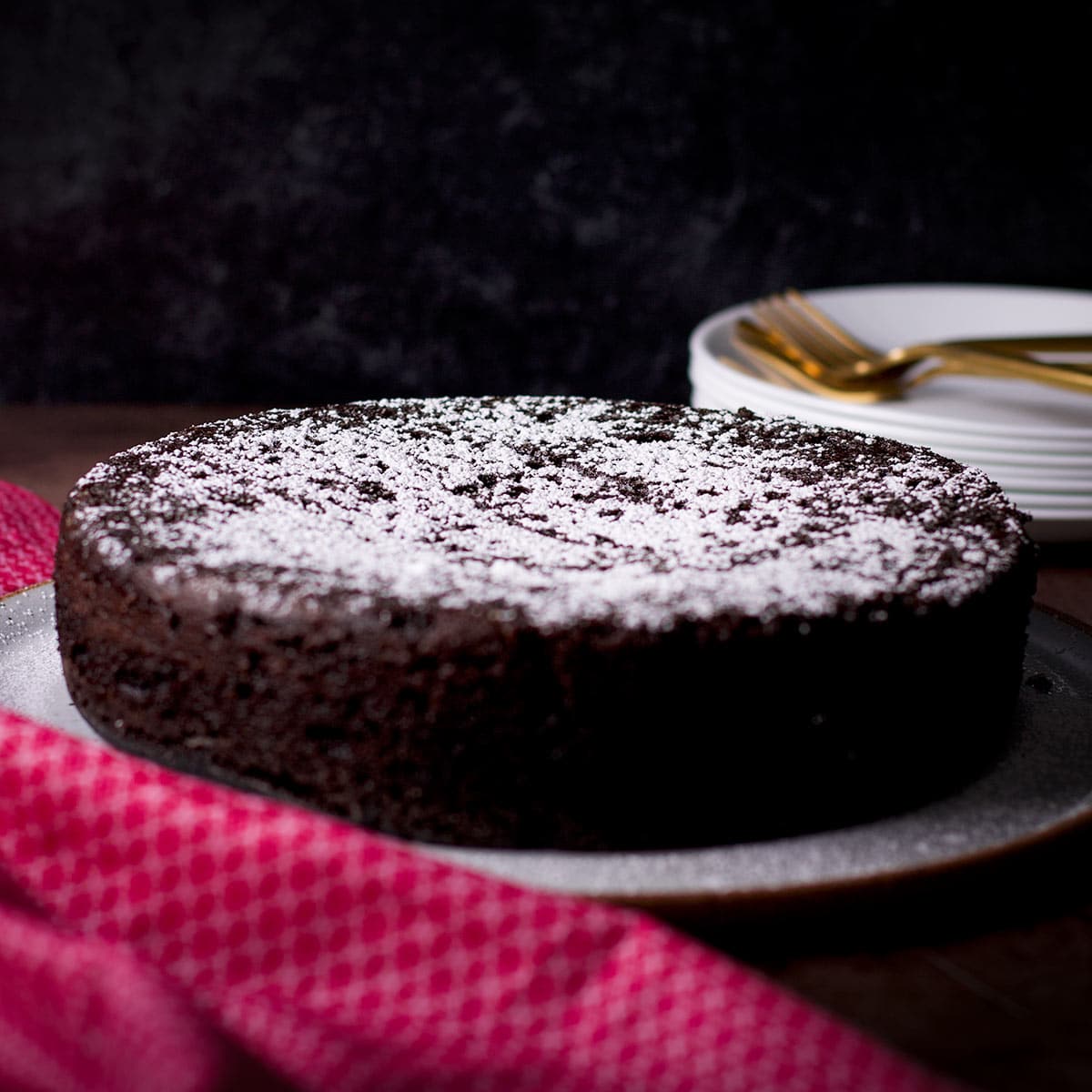 A Dutch oven chocolate cake covered in powdered sugar on a white serving platter.