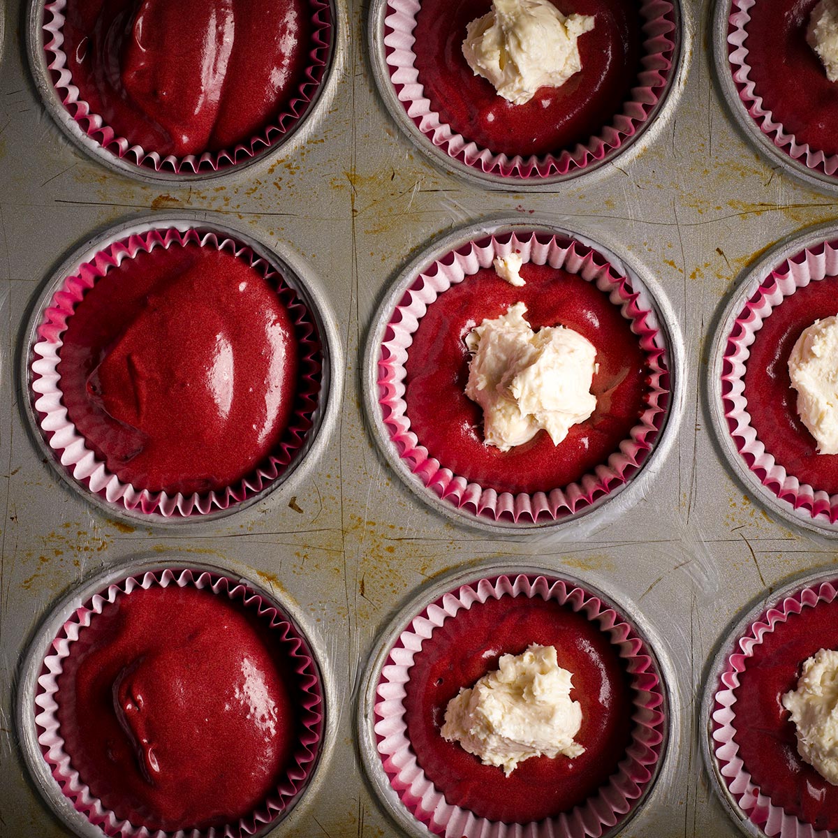 A muffin tin lined with paper liners and filled with red velvet muffin batter. 