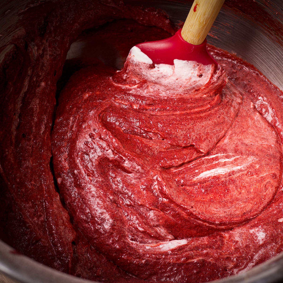 Using a rubber spatula to gently fold whipped cream into red velvet muffin batter. 
