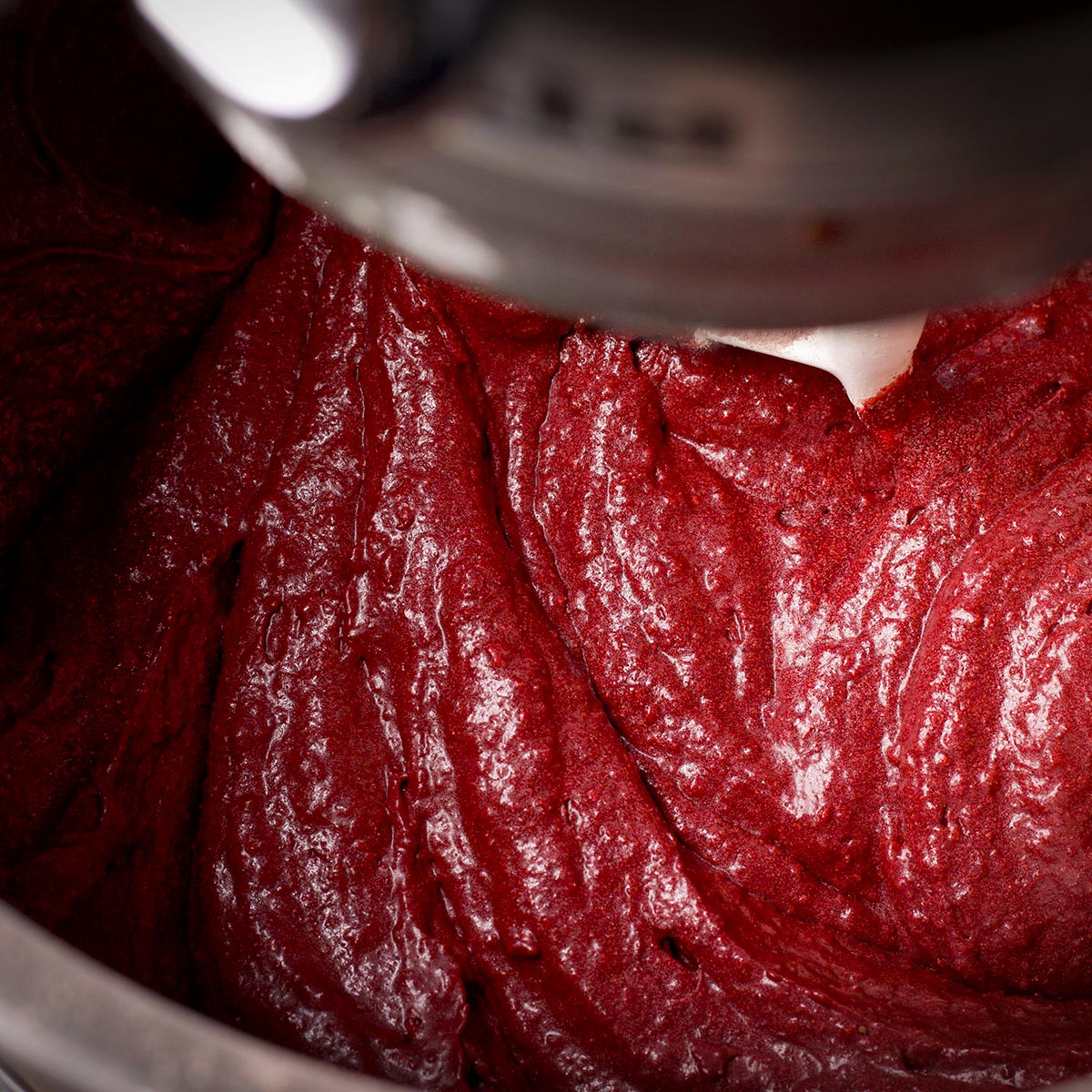 Using an electric mixer to beat the flour and buttermilk into the red velvet muffin batter. 