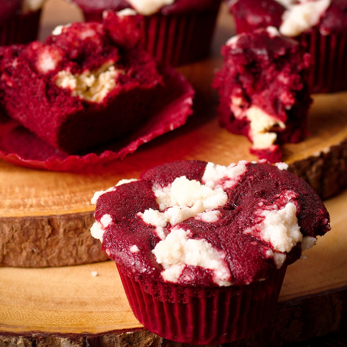 Several red velvet muffins with cream cheese filling and crumb topping on a wood serving board.
