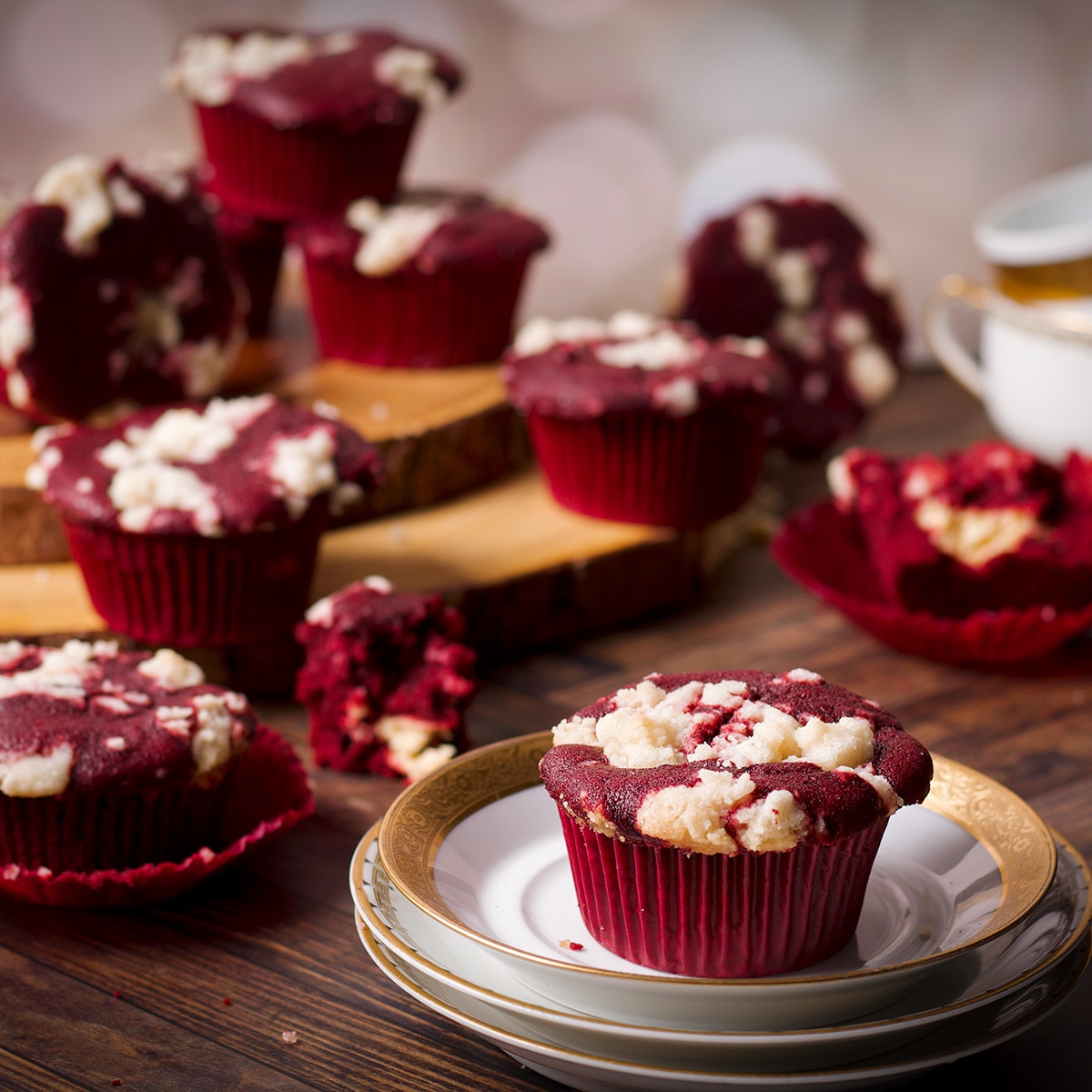 A cluster of red velvet muffins, some on a wooden tray, some on the table top, and one on a small white plate.