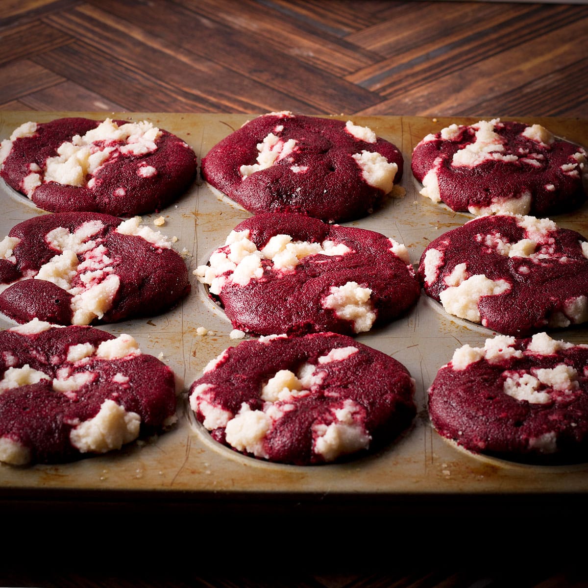 A freshly baked pan of red velvet muffins with a crumb topping.