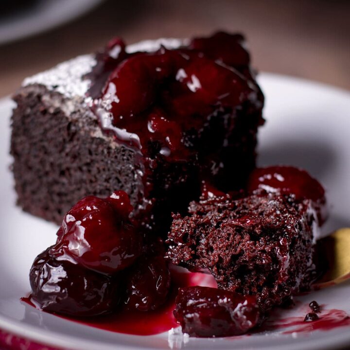 Using a fork to cut a bite from a slice of Dutch oven chocolate cake covered in cherry sauce.