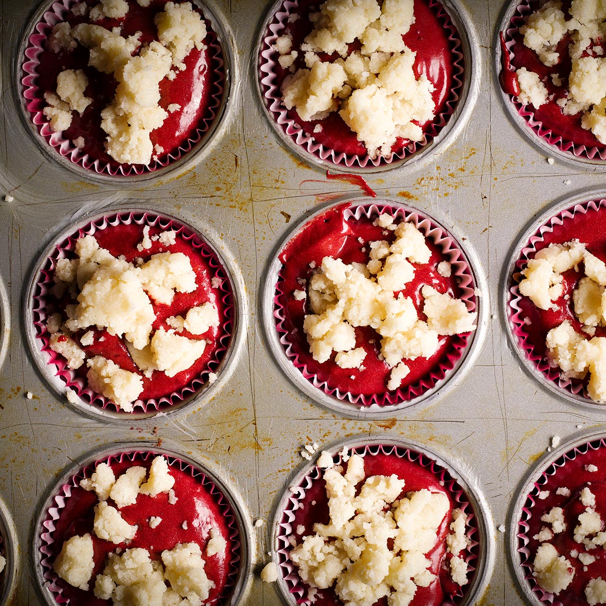 Top red velvet muffin batter with butter crumb topping before baking.