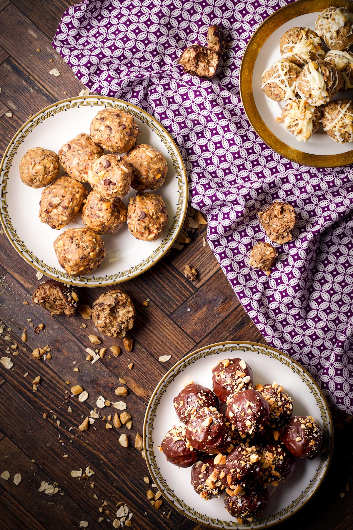 Three plates filled with different flavors of protein balls on a table with a purple cloth napkin.