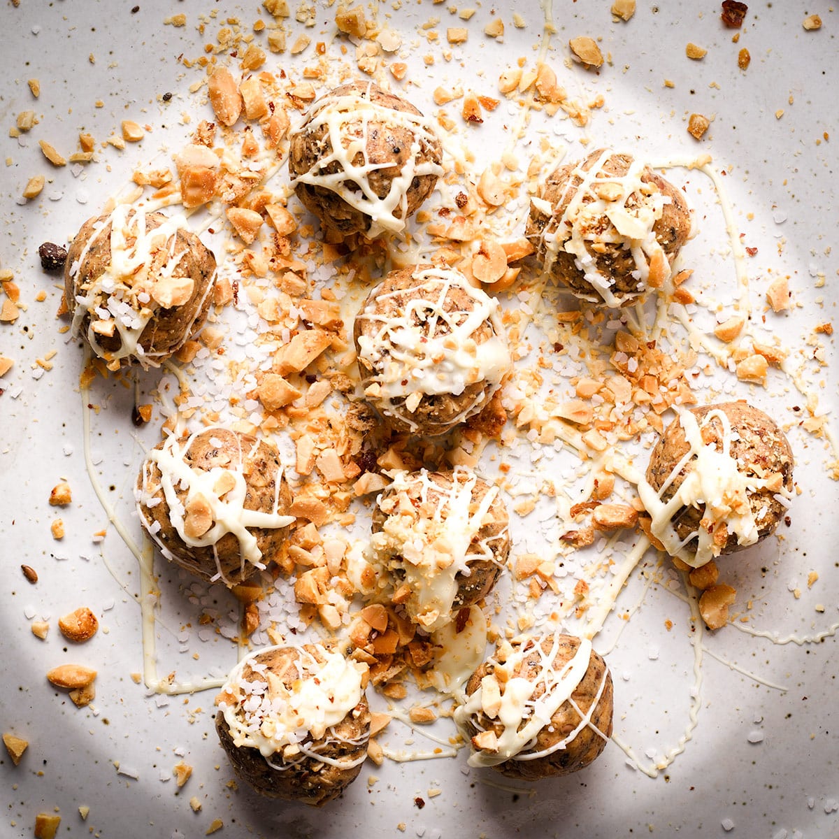 A plate of vanilla protein balls drizzled with melted white chocolate and covered with chopped peanuts.